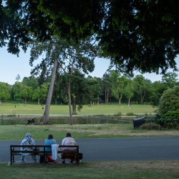 Three women sat on a bench looking out at the lake at Cannon Hill Park